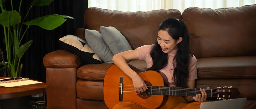 Beautiful young playing acoustic guitar, enjoying her weekend in cozy living room.