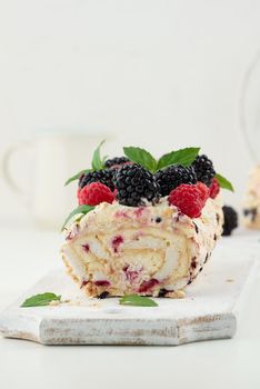 Baked meringue roll with cream and fresh fruits on a white wooden board, delicious dessert