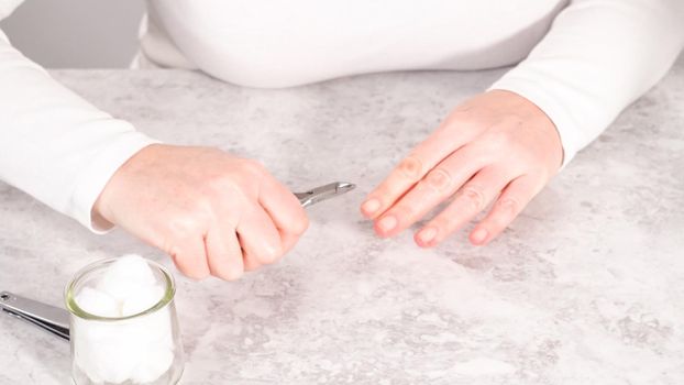 Woman finishing her manicure at home with simple manicure tools. Cutting out cuticles around the nails.