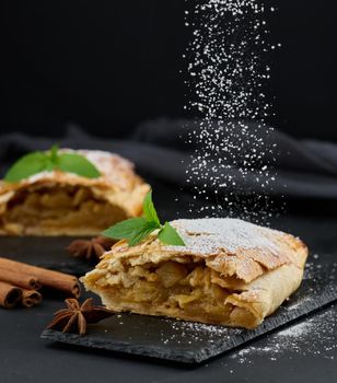 Baked strudel with apples sprinkled with powdered sugar on a black board, delicious dessert