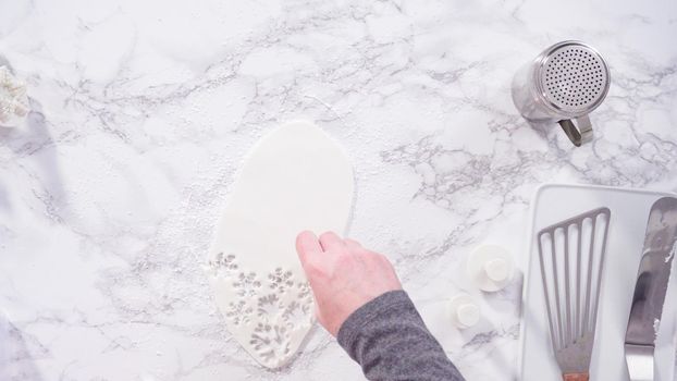 Flat lay. Step by step. Cutting out snowflakes with cookie cutters out of white fondant on a marble counter.