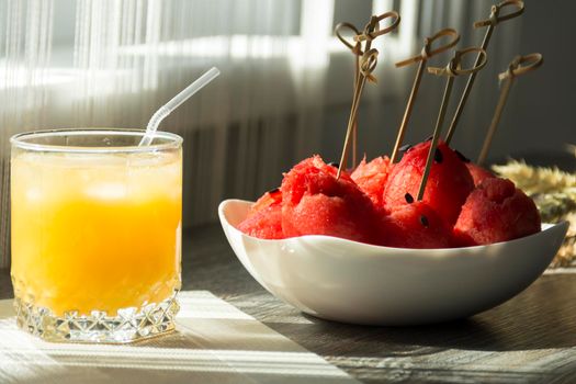 Freshly squeezed orange juice, sweet watermelon dessert and spikelets of ripe wheat on a wooden table in the sunlight...