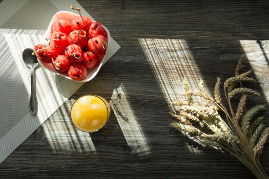 Freshly squeezed orange juice, sweet watermelon dessert and spikelets of ripe wheat on a wooden table in the sunlight...