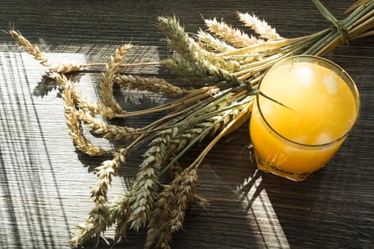 Freshly squeezed yellow juice and spikelets of ripe wheat on a wooden table in the sunlight.,,