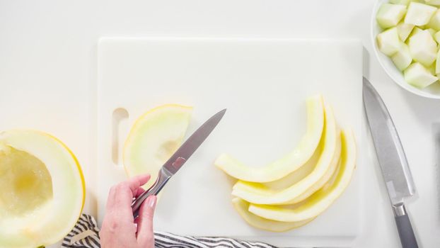 Step by step. Flat lay. Slicong golden dewlicious melon on a white cutting board.