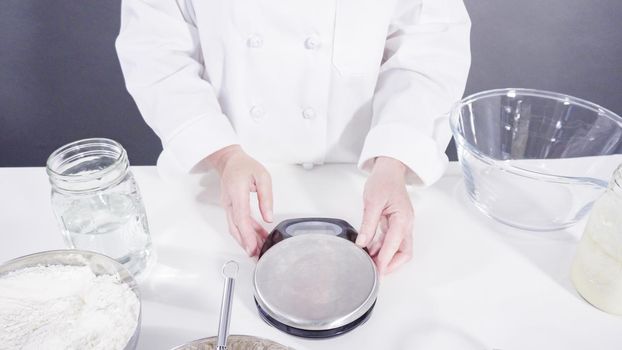 Measuring ingredients into a glass bowl to bake cinnamon rolls.