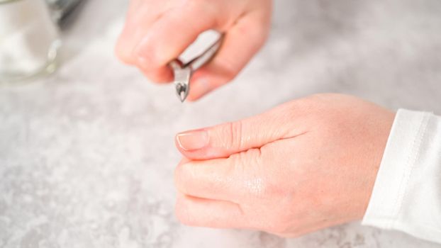 Woman finishing her manicure at home with simple manicure tools. Cutting out cuticles around the nails.