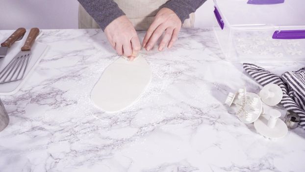 Step by step. Cutting out snowflakes with cookie cutters out of white fondant on a marble counter.