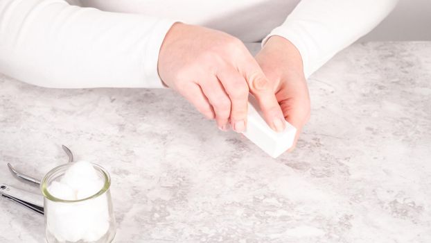 Woman finishing her manicure at home with simple manicure tools. Buffering nails with a nail buffer block.