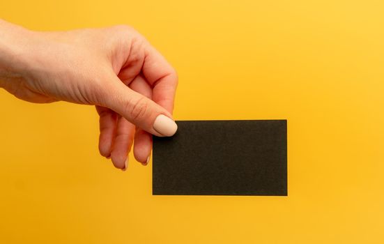 Black business card with copy space in female hand on yellow background mockup. Identity branding blank for contact information and professional communication