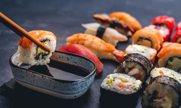 Person hold sushi maki roll with chopstick and put it to soy sauce. Oriental japanese healthy cuisine with rice and raw fish