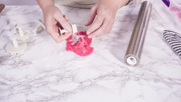 Step by step. Cutting out snowflakes with cookie cutters out of pink fondant on a marble counter.