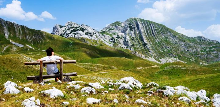 Girl sitting on wooden bench in mountains of Montenegro and looking back. Young girl resting in National park Durmitor with scenic nature view