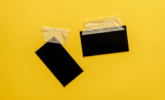 Black business cards with copy space attached with tape on yellow background. Identity blank for branding and professional communication