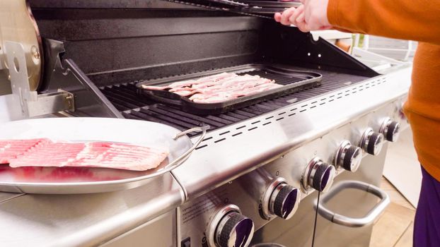 Cooking bacon stips on an outdoor gas grill.