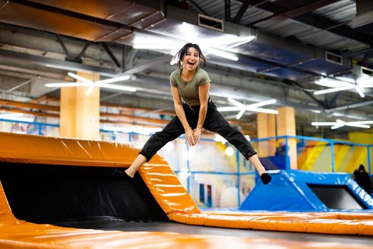 Pretty girl jumping on colorful trampoline at playground park, posing and laughing. Beautiful female teenager happy during active entertaiments indoor