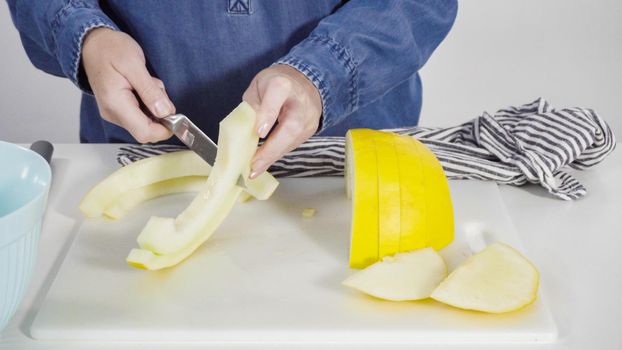 Step by step. Slicong golden dewlicious melon on a white cutting board.