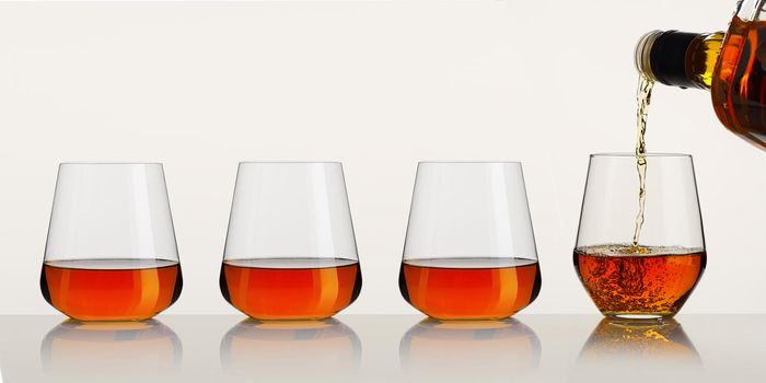 Pouring whisky from a bottle. whiskey being poured into a glass from bottle on white background. strong alcohol brandy, Cognac