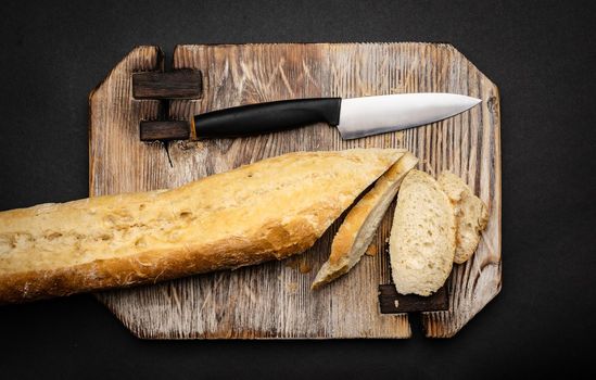 French baguette for bruschettas sliced with knife on wooden board closeup. Rustic crusty bread loaf for teraditional snacks