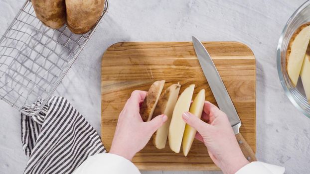 Flat lay. Step by step. Slicing russet potatoes in wedges with olive oil and spices to bake in the oven.