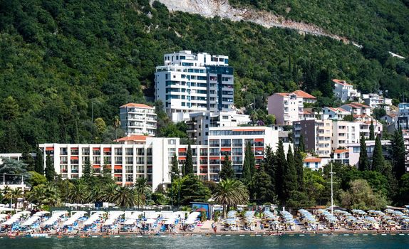 Modern Mediterranean city in Montenegro with hotels and beach, view from Adriatic sea. Luxury resort with beautiful coastline and mountains on background