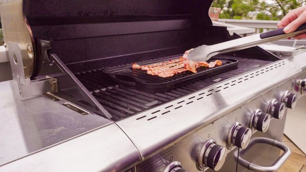 Cooking bacon stips on an outdoor gas grill.