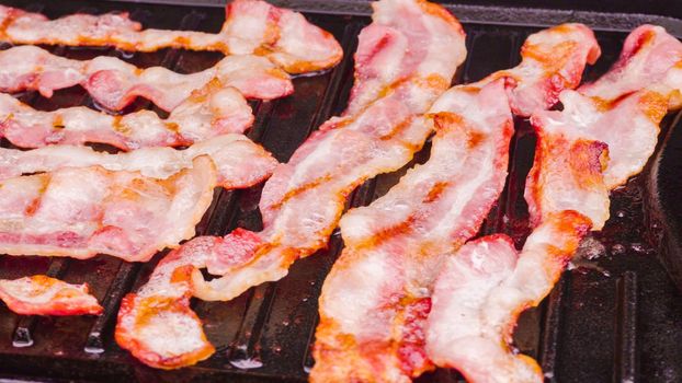 Cooking bacon stips on an outdoor gas grill.