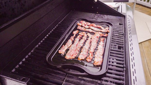 Cooking bacon stips on an outdoor gas grill.