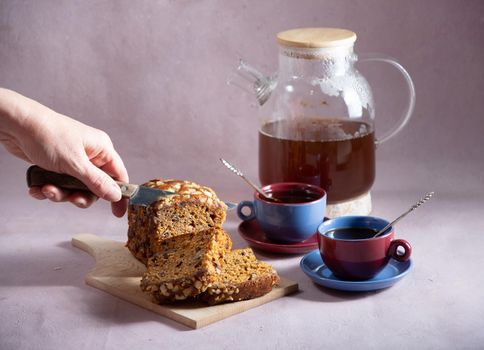 a female hand attacks a brown cupcake with candied fruit for breakfast, a beautiful ceramic cup and coffee in a teapot