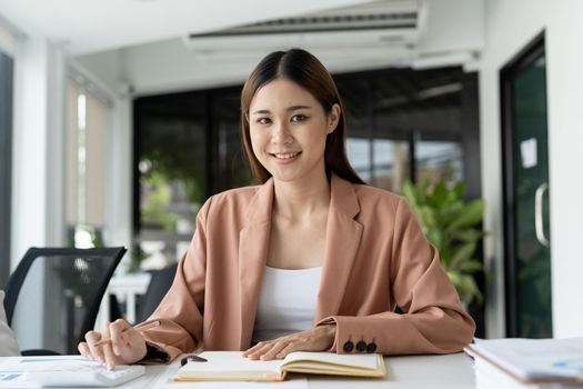 Image of a charming asian woman working calculator at a modern office. looking at camera