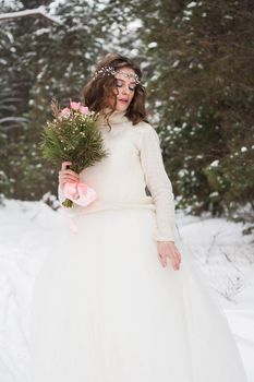 Beautiful bride in a white dress with a bouquet in a snow-covered winter forest. Portrait of the bride in nature.