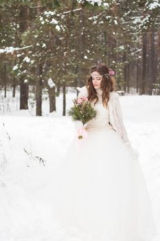 Beautiful bride in a white dress with a bouquet in a snow-covered winter forest. Portrait of the bride in nature.