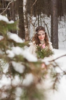 Beautiful bride in a white dress with a bouquet in a snow-covered winter forest. Portrait of the bride in nature.