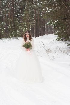 Beautiful bride in a white dress with a bouquet in a snow-covered winter forest. Portrait of the bride in nature.