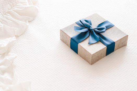 Holiday present and luxury online shopping delivery, wrapped linen gift box with blue ribbon on bed in bedroom, chic countryside style, close-up