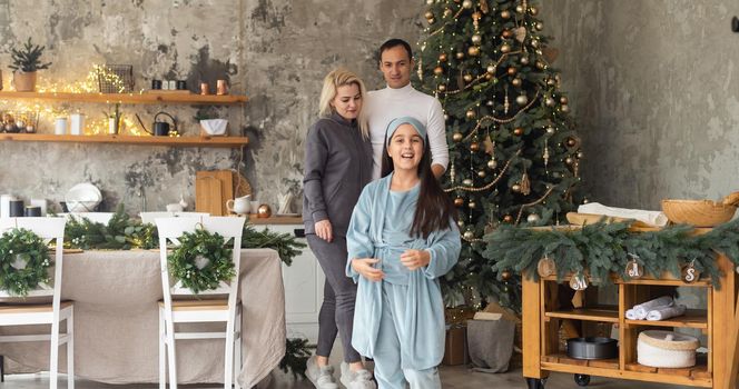 beautiful Christmas tree at home. Parents presenting gift box to charming daughter