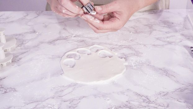 Step by step. Cutting out snowflakes with cookie cutters out of white fondant on a marble counter.