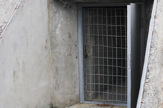 Open door to the cellar with bars in an old stone building.