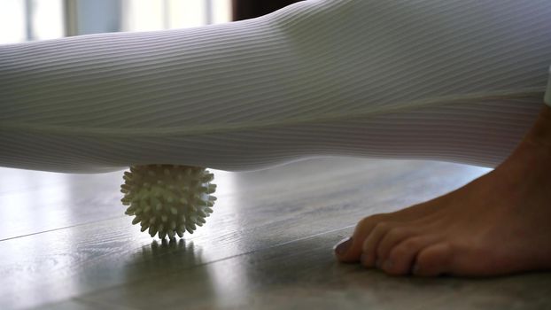 Athletic slim caucasian woman doing thigh self-massage with a massage ball indoors. Self-isolating massage.