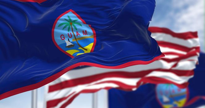 Flags of Guam waving in the wind with the US flag on a clear day. Guam is an organized, unincorporated territory of the United States in the Micronesia subregion of the western Pacific Ocean