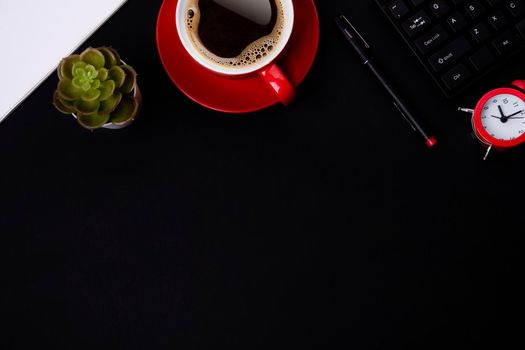 red cup of coffee, pen, glasses, alarm, plant, phone, and paper on a black background as workplace top view space for text