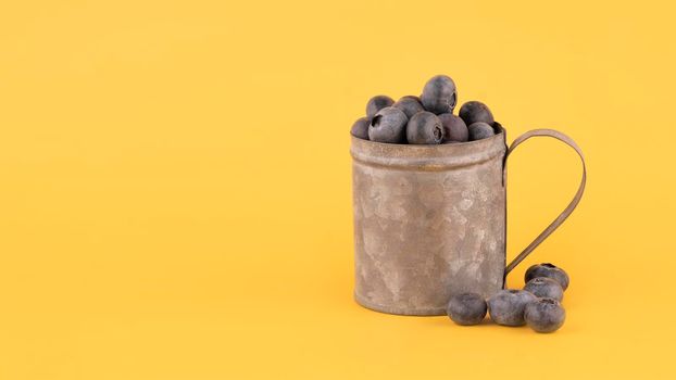 fresh blueberries in a cup on yellow background Copy space