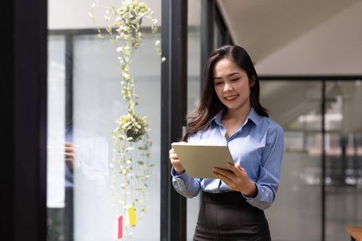 Business asian woman using digital tablet standing near window at office