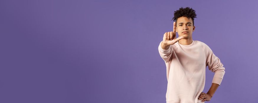 Not so fast, stop. Portrait of young serious-looking hispanic elder brother scolding sibling, forbid coming outside, shaking finger with serious confident face, prohibit action, purple background.