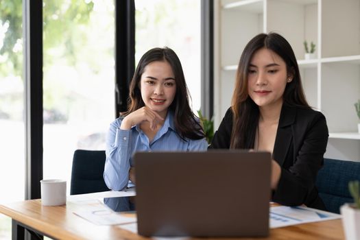 two young asian woman working on laptop computer at office