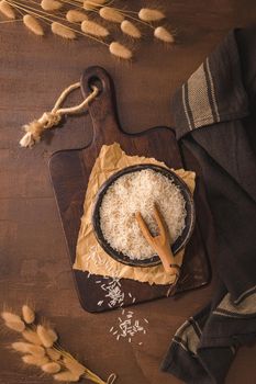Long grain rice in ceramic bowl with wooden scoop on rustic countertop.