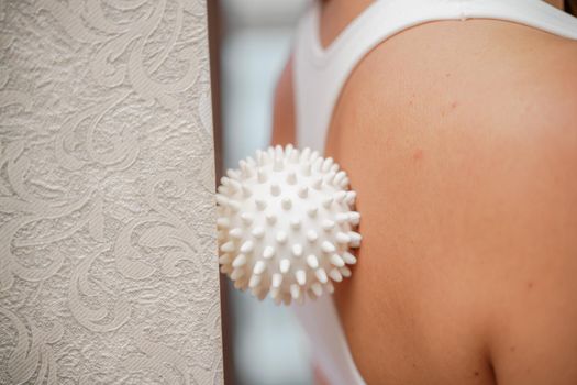 Athletic slim caucasian woman doing thigh self-massage with a massage ball indoors. Self-isolating massage.