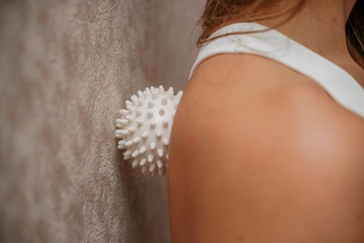 Athletic slim caucasian woman doing thigh self-massage with a massage ball indoors. Self-isolating massage.