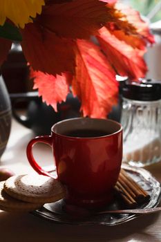 Red cup of tea on metal plate with red colored leaves, cookies and cinnamon sticks,on white wooden table, autumn morning concept, still life, selective focus, clpse up.