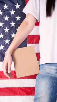 Young woman holds empty cardboard with Space for Text sign against American flag on background. Girl protesting anti-abortion laws. Feminist power. Womens rights freedom